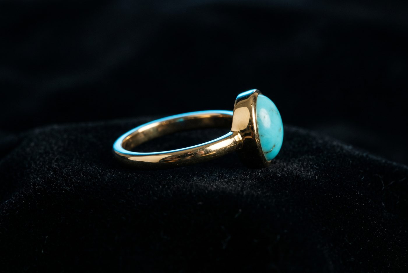 Low-profile bezel-set cabochon ring in yellow gold, side view, neutral backdrop