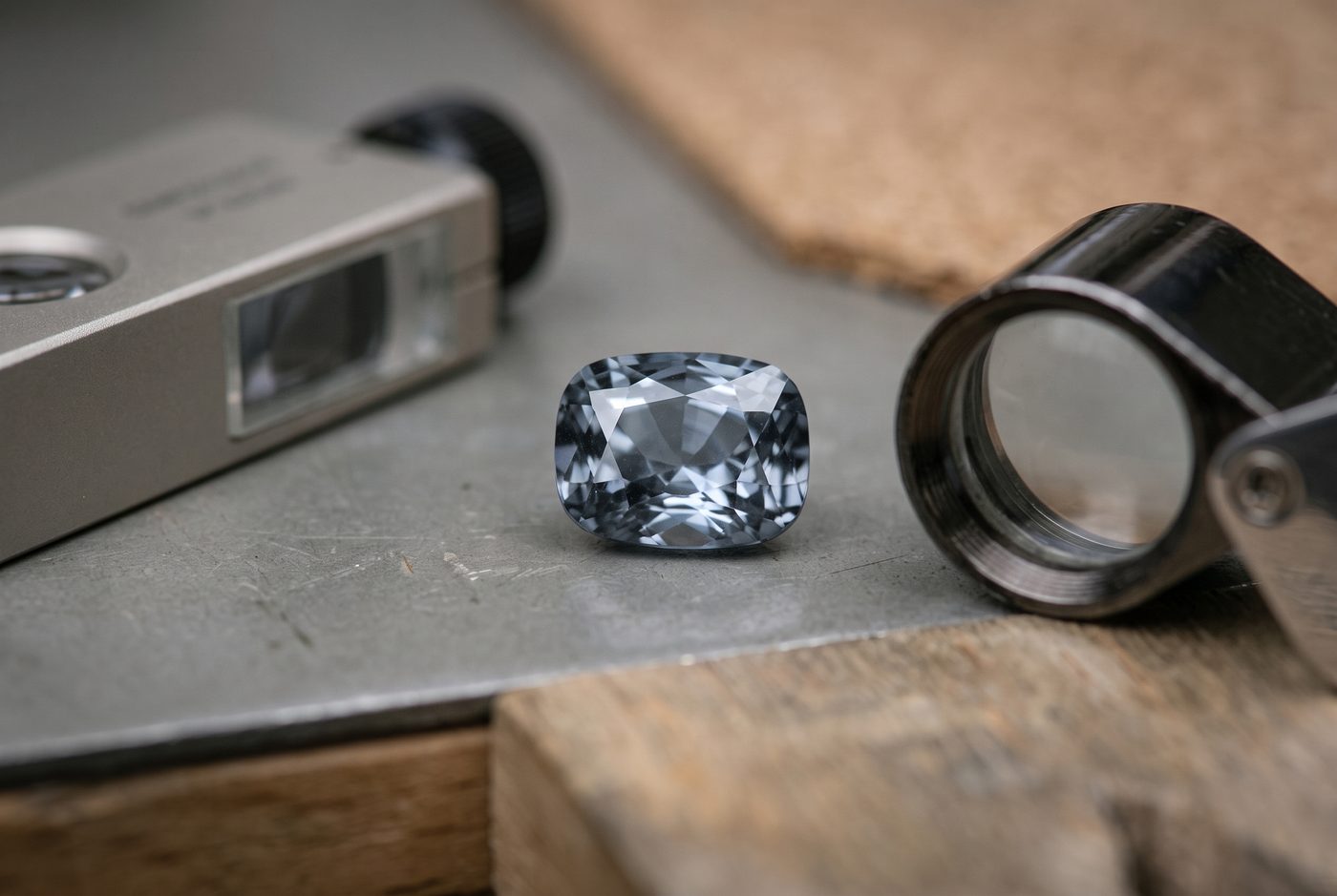 Grey faceted gemstone beside a refractometer and loupe on a neutral gemmologist's bench