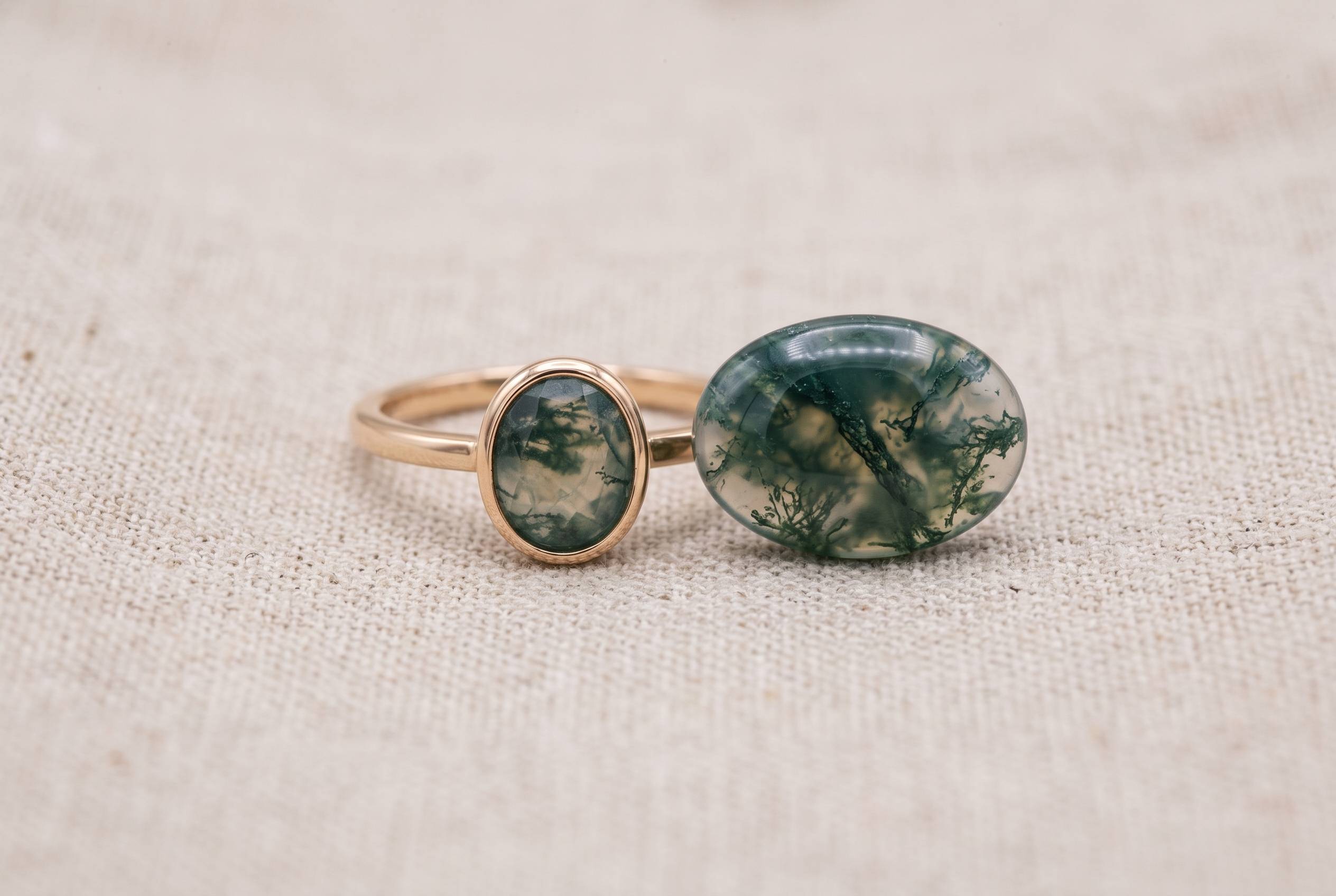 Low-profile bezel-set moss agate ring beside loose cabochon on neutral linen surface