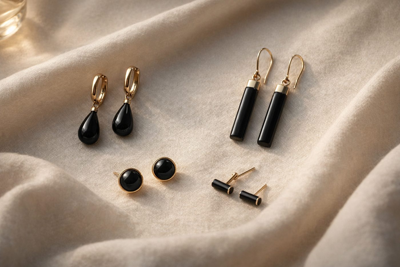 a collection of minimalist onyx earrings displayed on a soft fabric background