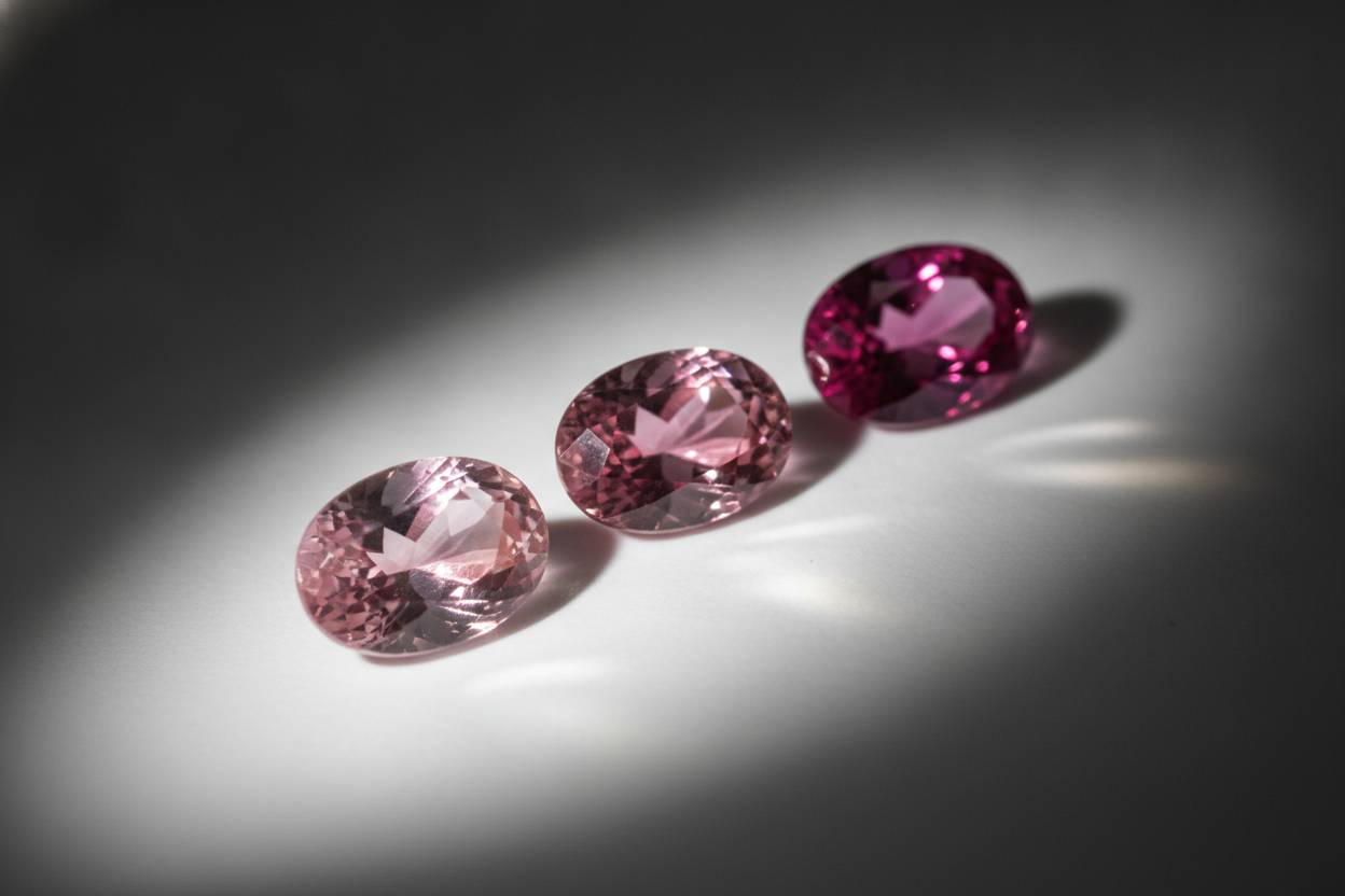 Three loose pink sapphires graded light to strong saturation on matte white surface